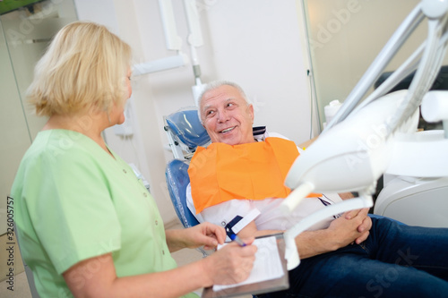Dentist female talking with smile senior man patient in dental clinic. Dental care for elder people. Dentistry, medicine and health care concept