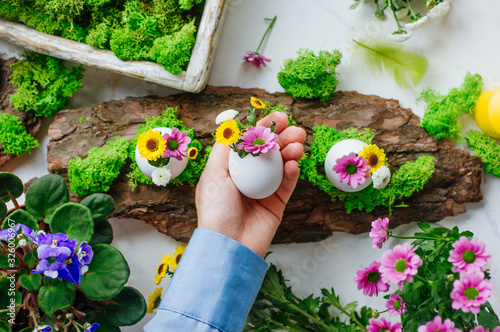 Female hand holding Easter decorted egg with golden-daisy flowers