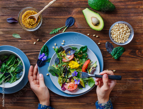 Fotografia Young woman eating fresh healthy salad with edible flowers