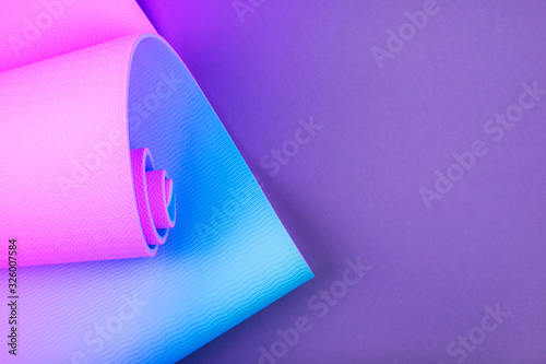 Top view of neon colored blue pink yoga mat on violet background. Yoga pilates sport concept. Flat Lay.