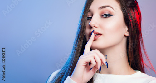 portrait of cocky teenager girl with long hair on coloured studio background, young woman face with finger near lips, fashion model, female beauty