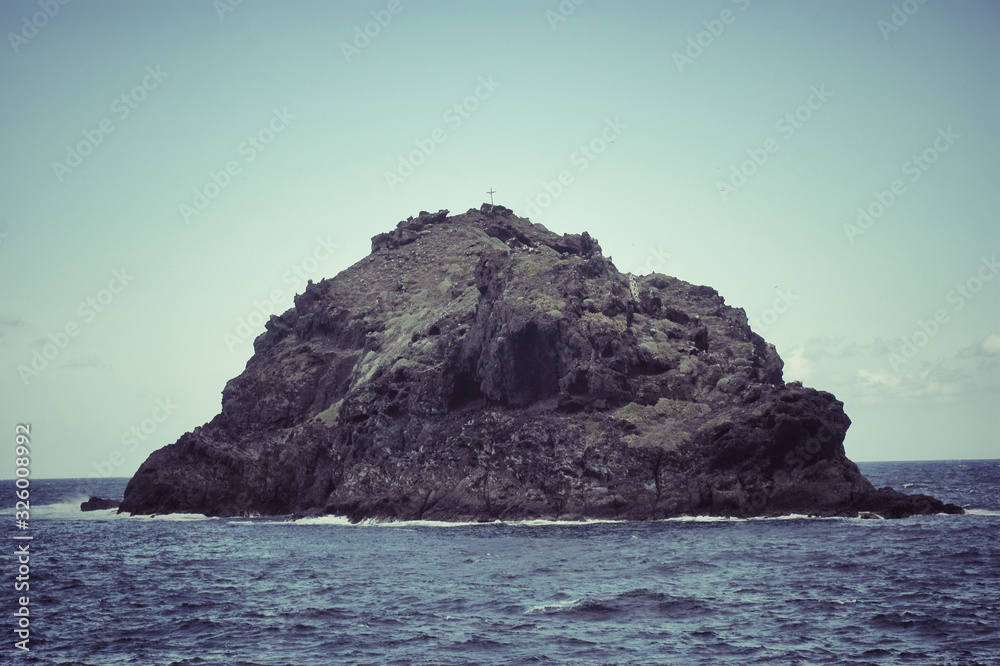 A lonely little island in the ocean with a cross on top.