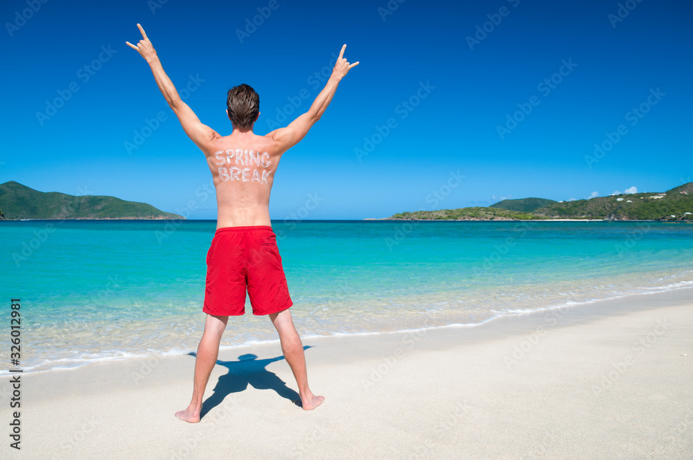 Dude with Spring Break written in sunscreen on his back rocking out with his hands in the air on a tropical beach Dude with Spring Break written in sunscreen on his back rocking out with his hands in the air on a tropical beach