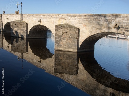 Old stone bridge with arches and statues and its reflection on the surface of the river photo