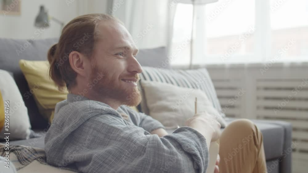 Close up of Caucasian man with red hair wearing comfortable clothes sitting in living room, eating Asian food from box while watching television Close up of Caucasian man with red hair wearing comfortable clothes sitting in living room, eating Asian food from box while watching television