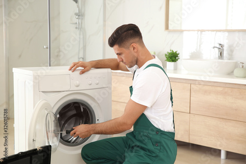 Professional plumber repairing washing machine in bathroom