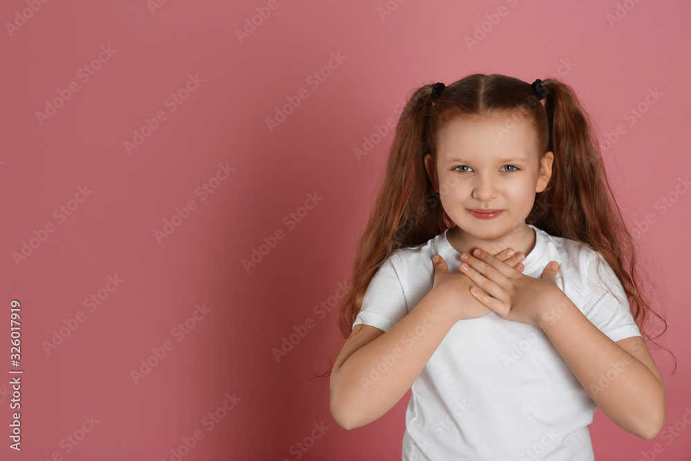 Cute grateful little girl with hands on chest against pink background. Space for text Cute grateful little girl with hands on chest against pink background. Space for text