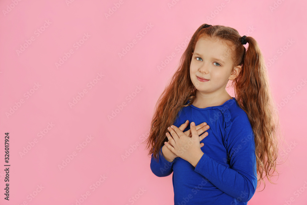 Cute grateful little girl with hands on chest against pink background. Space for text Cute grateful little girl with hands on chest against pink background. Space for text