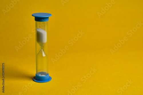 Blue hourglass or sandglass at yellow background. Time management concept