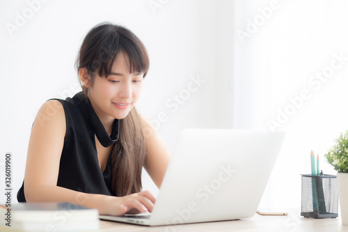 Beautiful freelance asian woman smiling working and typing on laptop computer at desk office with professional, girl using notebook checking email or social network, business and lifestyle concept. © N_studio