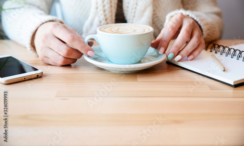 Cup of coffee and woman's hands with phone and notebook on a wooden table with copy space. Freelance and business meeting. Banner.