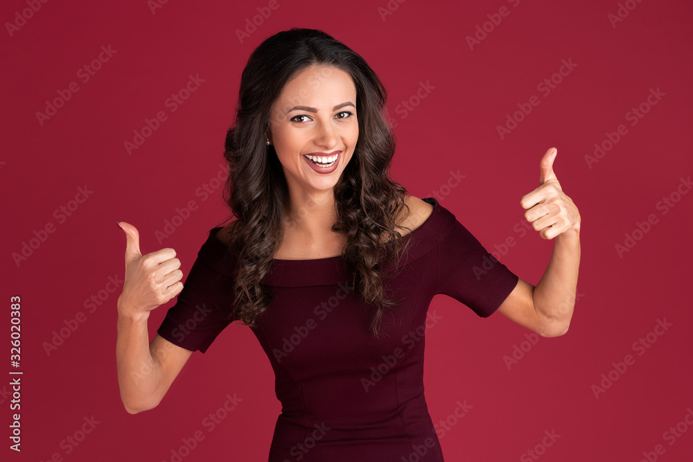Cheerful young woman in maroon dress show ok gesture over red background. Cheerful young woman in maroon dress show ok gesture over red background.