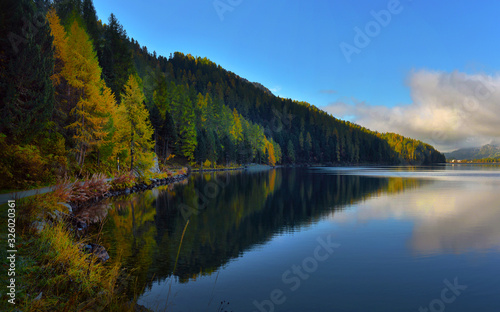 Mountain lake at sunrise in autumn. Landscape with lake, gold sunlight, blue fog over the water, reflection, trees with colorful leaves