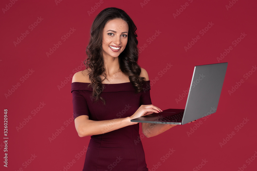 Fototapeta premium Beautiful elegant young woman in maroon dress use notebook or computer over red background.