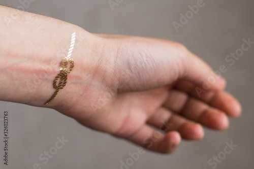 hand of a young woman wih gold sailors knot temporary tattoo on her wrist