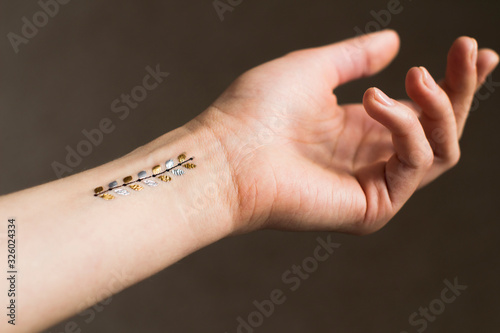 hand of a young woman wih gold floral leaves temporary tattoo on her wrist