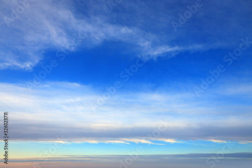 Blue sky background with light white clouds at the zenith and long stripes of clouds on the horizon.