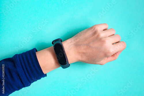 Classic blue fitness bracelet for sports training on a girls hand on mint background. Selective focus.