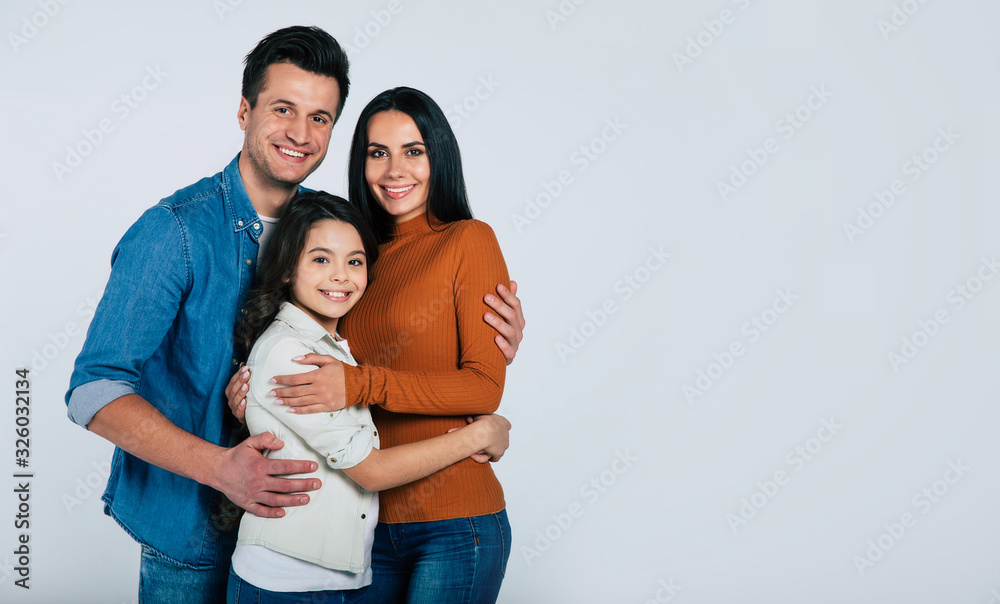 Family picture. Close-up photo of a young family of mother, father, and daughter, standing together in casual outfits and smiling. Family picture. Close-up photo of a young family of mother, father, and daughter, standing together in casual outfits and smiling.