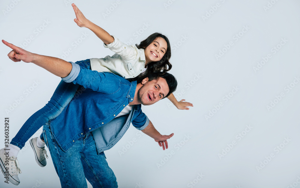 The funniest time. Cheerful young father is giving a back ride to his small cute daughter, who is imitating a plane, while they are both laughing and goofing around. The funniest time. Cheerful young father is giving a back ride to his small cute daughter, who is imitating a plane, while they are both laughing and goofing around.