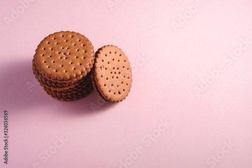Chocolate sandwich cookie with cream, sweet stacked food from store, on pink pastel background, angle view