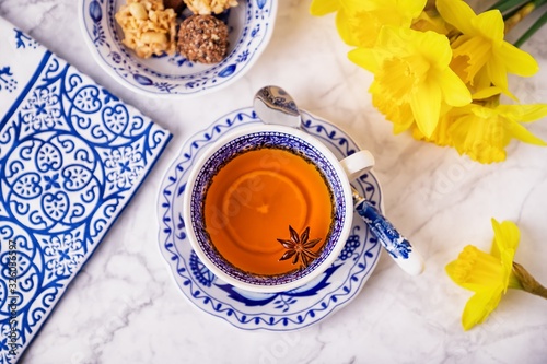 A cup of lemon tea with anise star. White and blue dishes and yellow daffodils. Top view