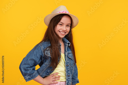 Cheerful fashionable girl in hat and denim jacket looking at camera