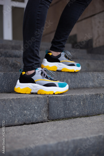 Feet shod in multi-colored sneakers of yellow, white, black and blue on the marble stairs