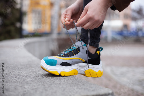 Girl tying shoelaces on multi-colored sneakers of yellow, white, black and blue on the street photo