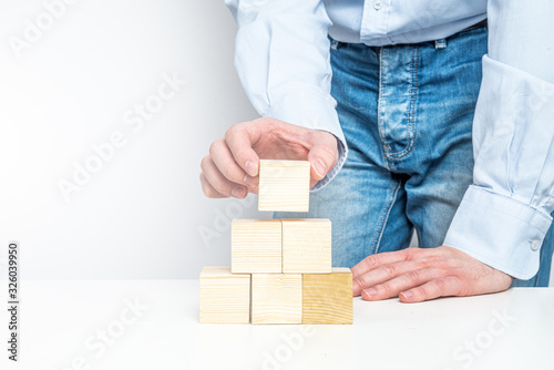 Stacking wooden blocks without content. Business concept, content supplementation. A man arranges blank wooden blocks one on top of the other, creating a concept.