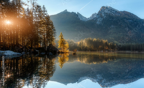 Awesome alpine lake during sunset. Scenic image of fairy-tale Landscape in sunlit with Majestic Rock Mountain on background. Wild area. Hintersee lake. Germany. Bavaria  Alps. Creative image