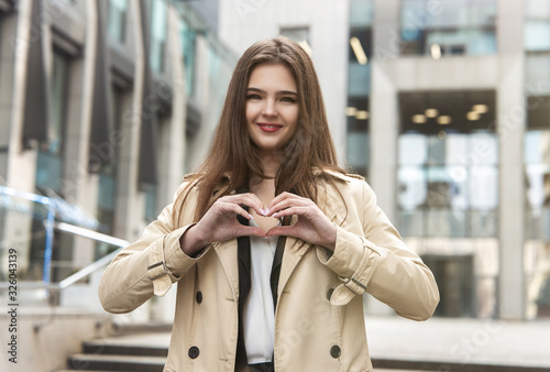 stylish young businesswoman wearing smart outfit stands in the middle of the street showing heart with her hands, body language concept, love and care