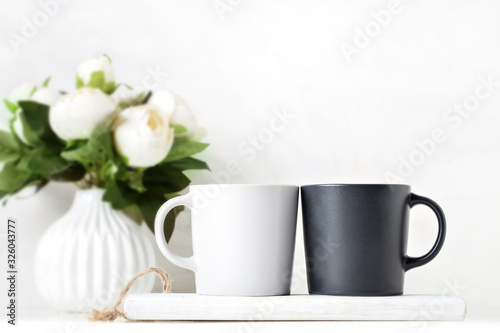 White and black mugs on a background of flowers . Mock up. Template Space for Creative Artwork Lettering Text Product Promotion Branding. Elegant style.