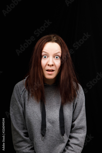 Young woman is surprised. The girl wear casual grey jacket on a black background. 