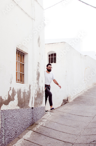 erudite young person with a beard and glasses carries books and walks through the old streets of a town © javiemebravo