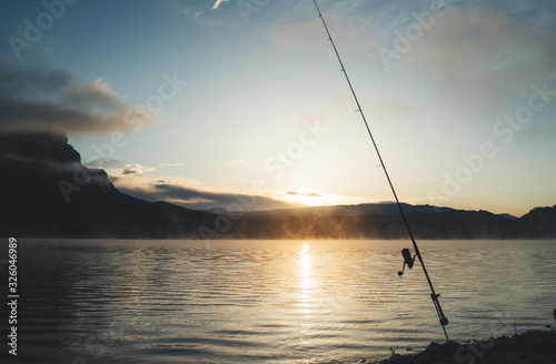 fishery relax concept  outline fishing rod at sunrise sunlight  hobby sport on mist evening lake  catch fish on river on background night sky foggy mount