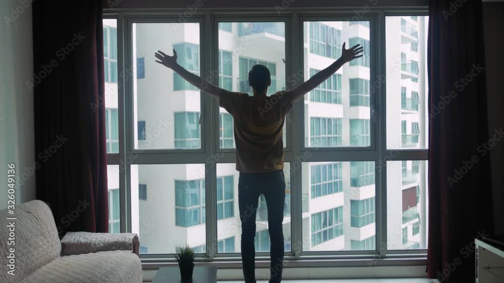 Silhouette of young man looking at window of the room and rising hands up hands. The concept of dreams and success. Silhouette of young man looking at window of the room and rising hands up hands. The concept of dreams and success.