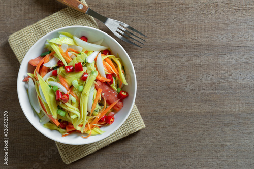 top view of spicy mango salad in a ceramic bowl on wooden table. asian homemade style food concept.