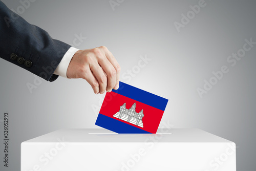 Man putting a voting ballot into a box with Cambodian flag.