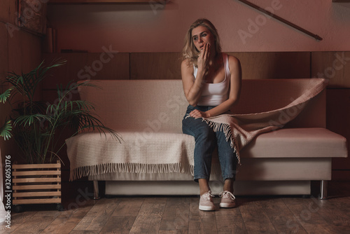 Woman touching face with bruise and sitting on sofa with blanket in room