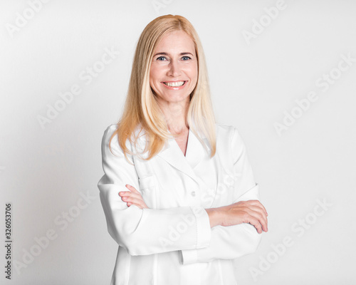 Happy middle-aged woman doctor in uniform crossing arms