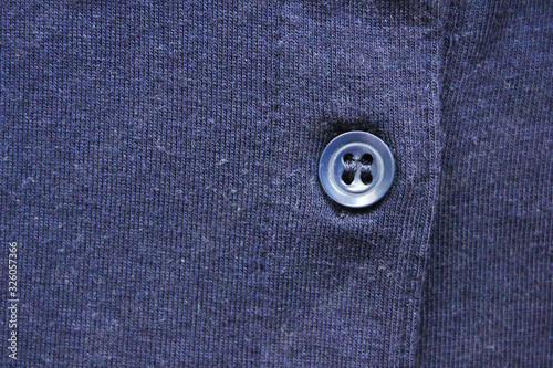 Button on dark blue cloth texture background. Simple button close up, blue cotton cloth material, casual clothes fabric top view 