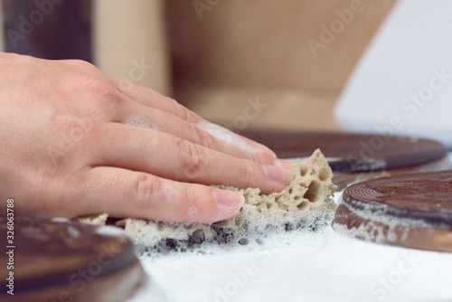 Woman is washing the surface of the electric stove with a cleaner close up.
