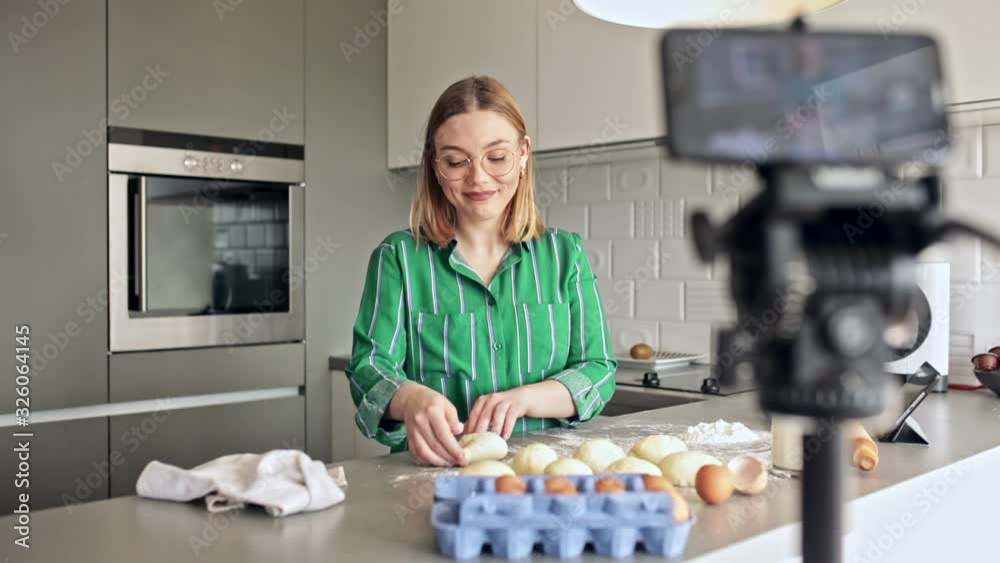 Young woman recording vlog at home in the kitchen preparing dough for pasta.