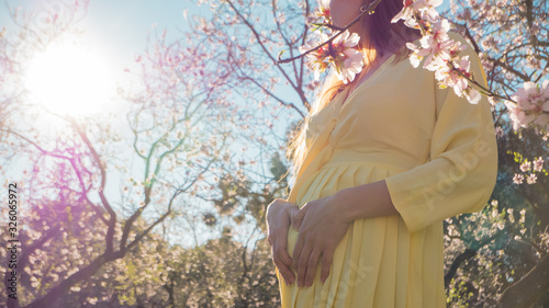 Beautiful pregnant woman maternity photoshoot in blooming early spring flowers with her hands in heart shape showing care and healthy lifestyle