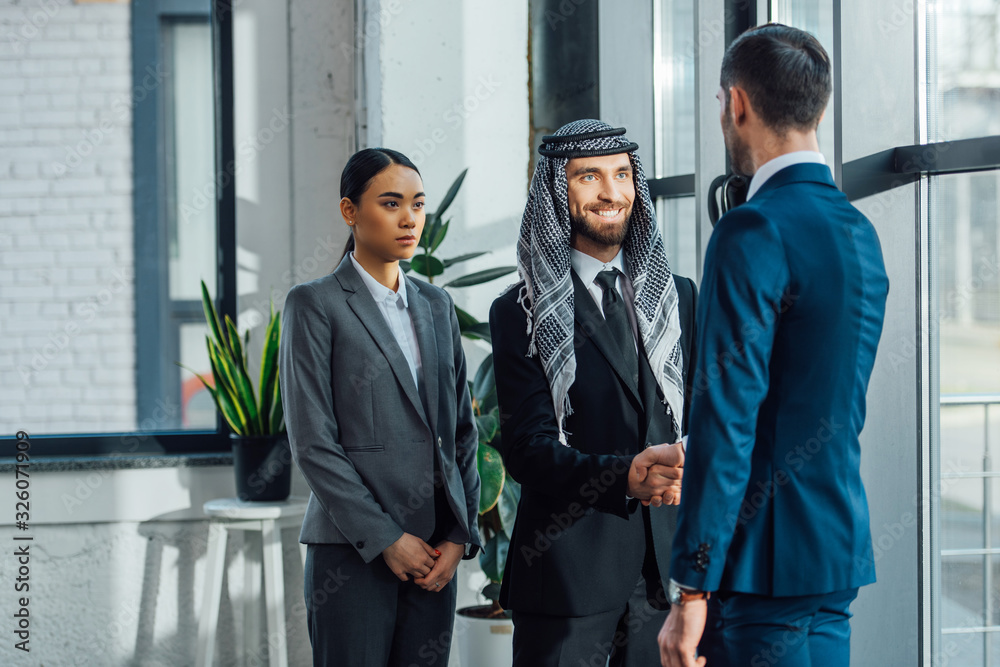 smiling multicultural business partners shaking hands and having deal with translator in office smiling multicultural business partners shaking hands and having deal with translator in office