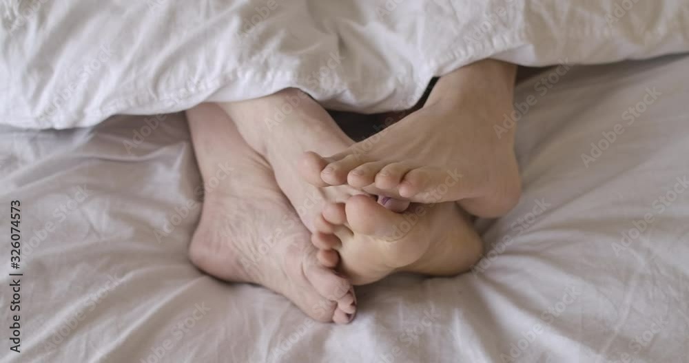 Close-up top view of senior female Caucasian feet touching male legs in bed, both pairs hiding under white blanket. Mature couple spending morning in bedroom. Romance, sex. Cinema 4k ProRes HQ. Close-up top view of senior female Caucasian feet touching male legs in bed, both pairs hiding under white blanket. Mature couple spending morning in bedroom. Romance, sex. Cinema 4k ProRes HQ.