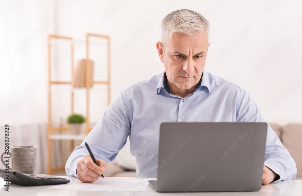 Senior man using laptop at office and writing notes Senior man using laptop at office and writing notes
