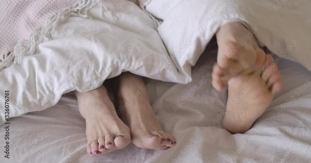 Close-up of male and female feet lying on bed sheets. Unrecognizable man scratching legs as woman lying quietly. Senior couple spending morning in bedroom. Lifestyle, leisure. Cinema 4k ProRes HQ. Close-up of male and female feet lying on bed sheets. Unrecognizable man scratching legs as woman lying quietly. Senior couple spending morning in bedroom. Lifestyle, leisure. Cinema 4k ProRes HQ.