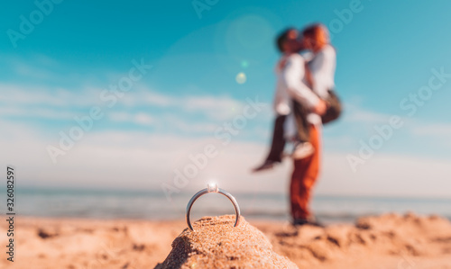 Romantic marriage proposal on the beach at the seaside. Couple in love kissing outdoor with a marriage ring in front of them. 